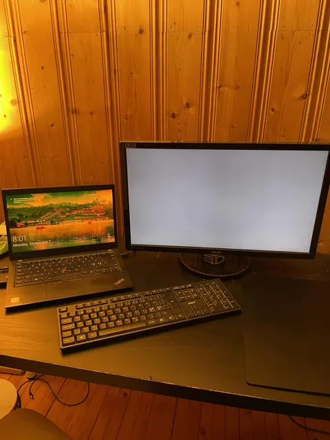 Der Schreibtisch des Machers: ein gebrauchter Laptop und ein Monitor auf einem Tisch in einem holzvertäfelten Keller.